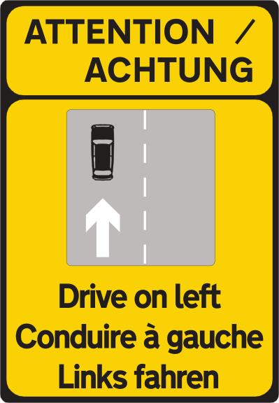 Yellow sign reading ATTENTION / ACHTUNG and Drive on left, with a small road diagram and French and German wording.