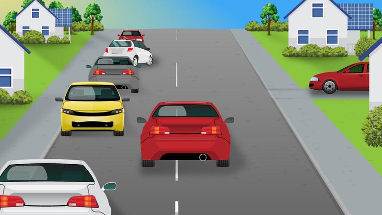 Red car ahead beside a line of parked cars on the left; another red car waits on a side road to the right.